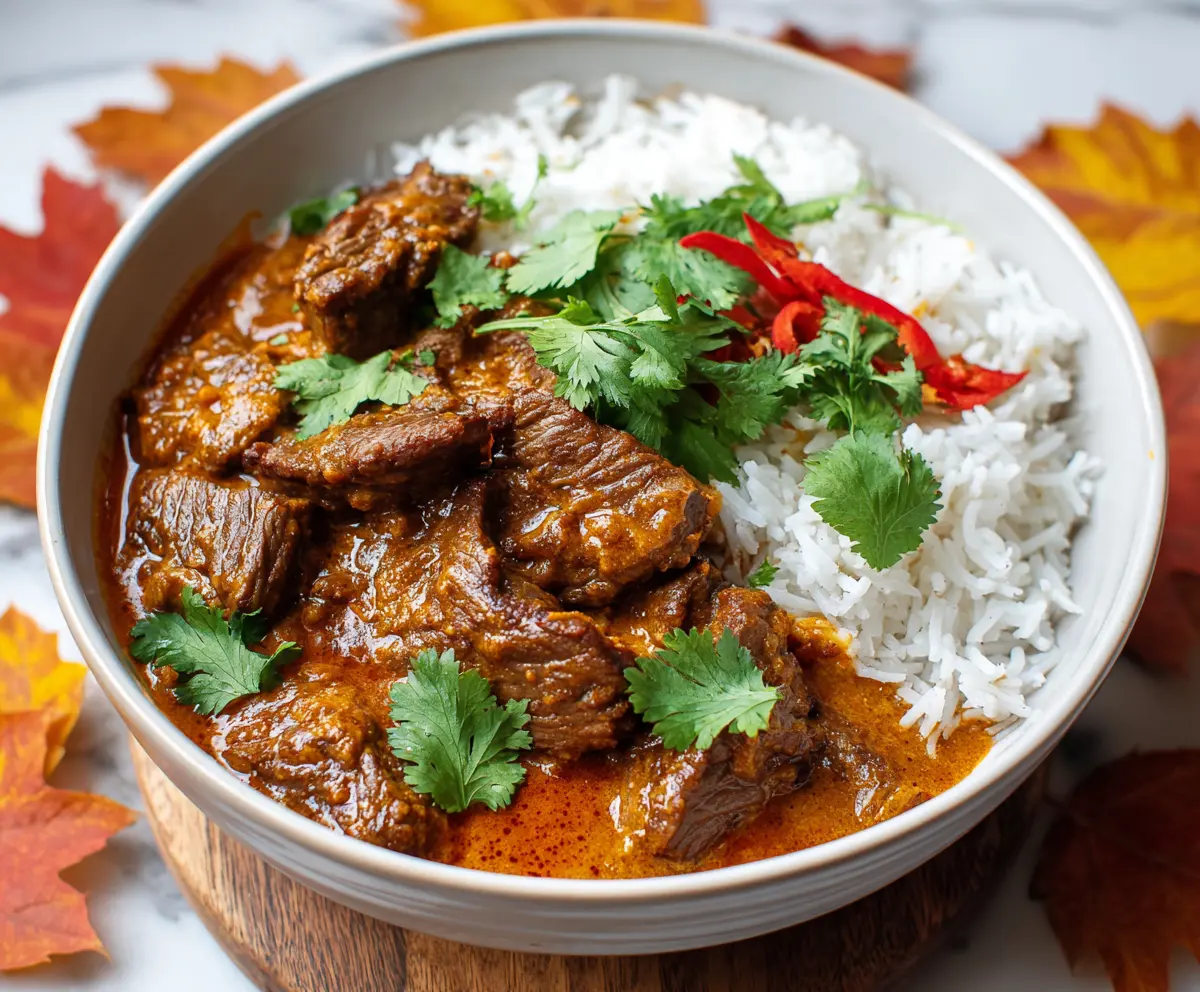 Delicious Slow Cooker Beef Coconut Curry in a bowl with fresh herbs and rice