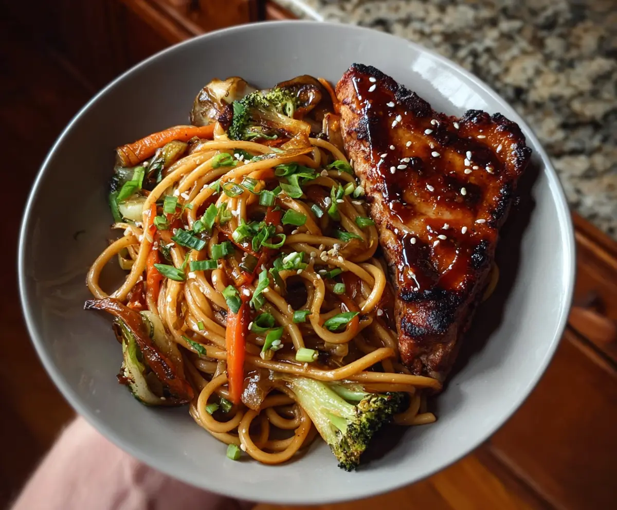 Delicious veggie udon noodles paired with sticky glazed pork chops on a vibrant plate.